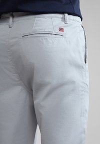 Pantalones gris claro hechos de tela tejida, con un bolsillo trasero y un pequeño acento de bandera noruega. Textura suave con un ajuste personalizado.