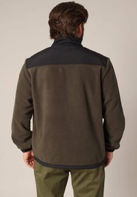 Fleecejas in olijfgroen met een zwarte nylon bovenkant, voorzien van een hoge kraag en elastische manchetten, met een gladde textuur en een relaxte pasvorm.