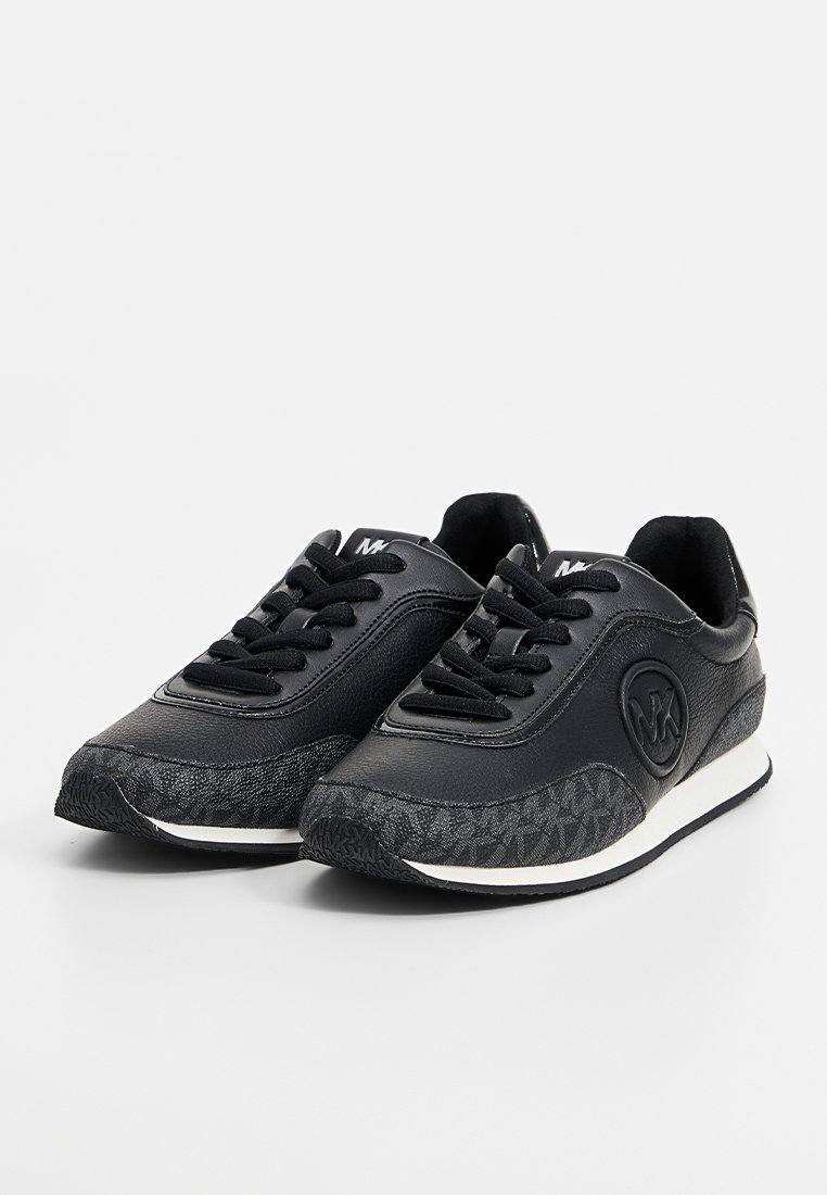 Zwarte lage sneakers met een textuur op de neus, zwarte veters, witte tussenzolen en een ronde merklogo op de zijkant.