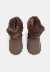 Bruna fluffiga tofflor med en mjuk fuskpälskrage, strukturerad filtövre och rund tåform, samt en flexibel sula. Perfekta för komfort och värme.