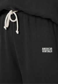Musta collegehousut pehmeästä kankaasta, joissa on valkoinen naru ja pieni valkoinen "AMERICAN VINTAGE" -logo edessä.
