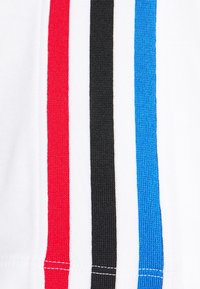 Bílá látka s vertikálními pruhy: červenou, černou a modrou. Textura se zdá být hladká s kontrastním barevným prošíváním podél okrajů.