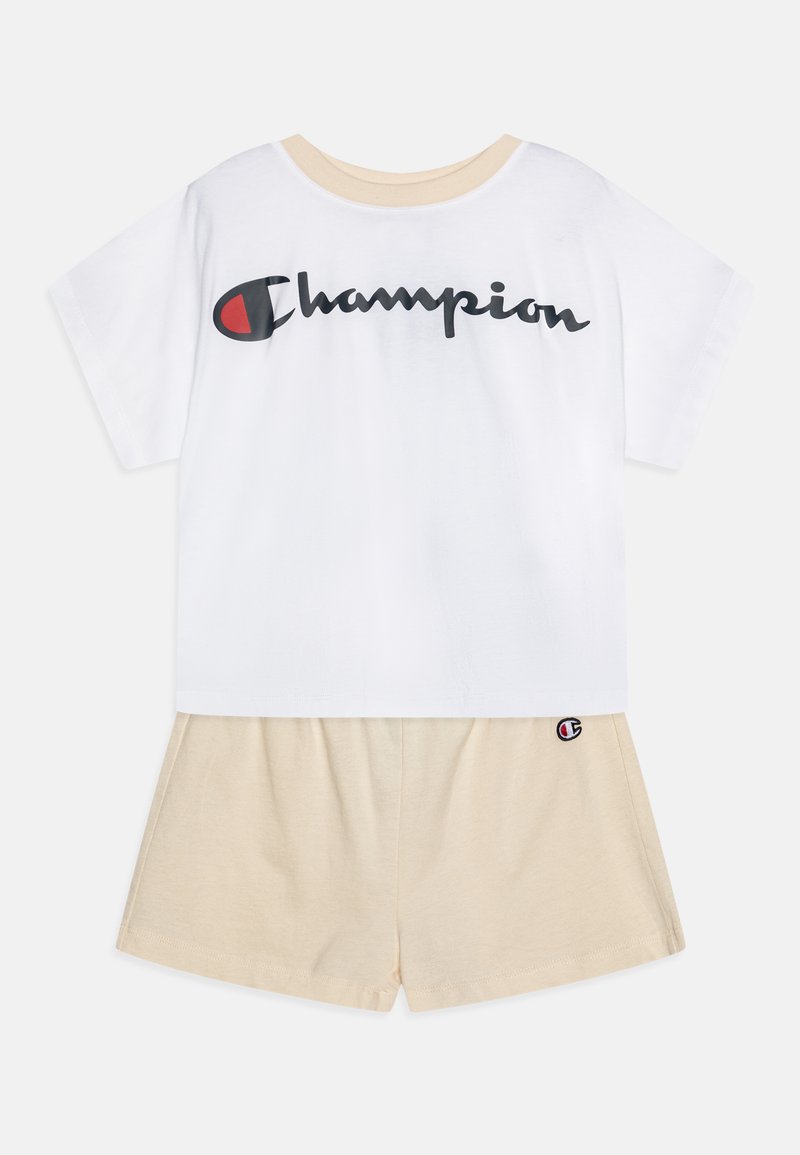 T-shirt bianca in cotone con logo "Champion" nero, abbinata a pantaloni corti beige in cotone con patch del logo sull'orlo. Fit classico e rilassato.