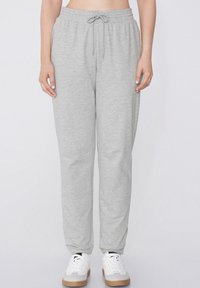 Pantalones de chándal grises con una cinturilla elástica y cordón, con un corte holgado y puños ajustados, combinados con zapatillas blancas.