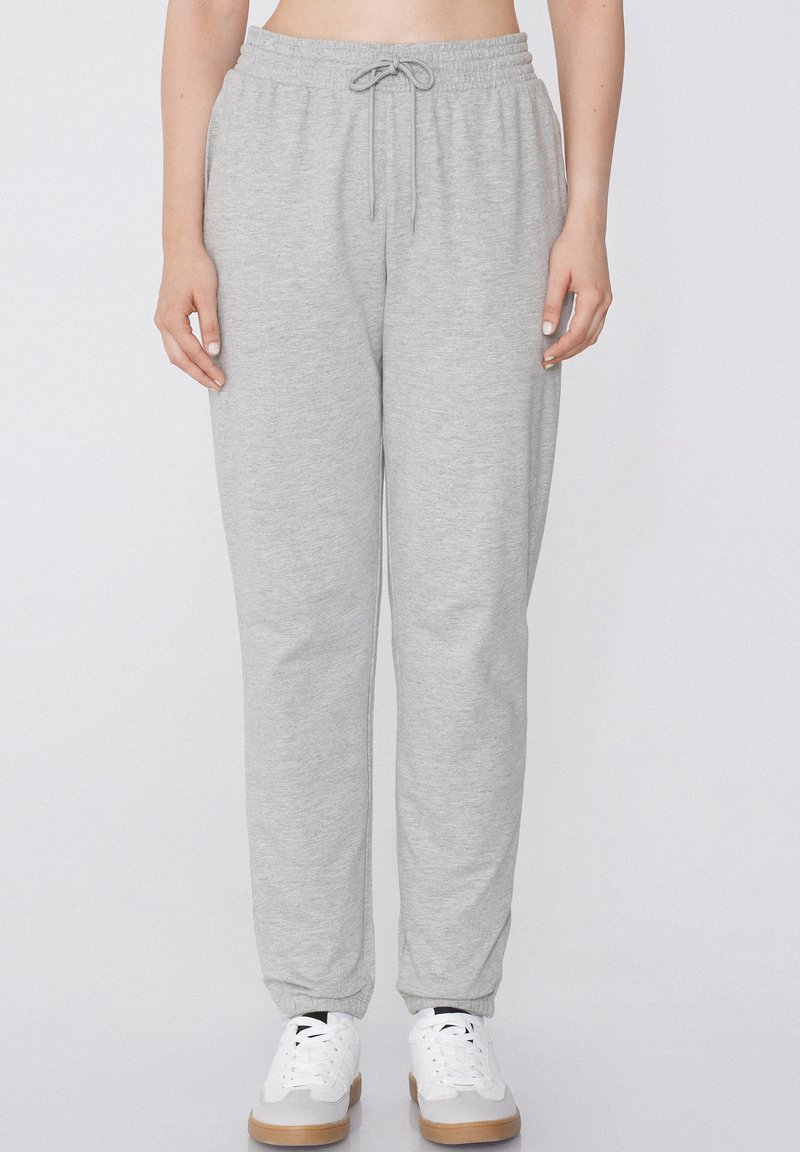 Pantalones de chándal grises con una cinturilla elástica y cordón, con un corte holgado y puños ajustados, combinados con zapatillas blancas.