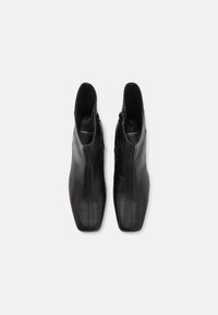 Botas de cuero negras hasta el tobillo con un diseño elegante, puntera afilada y cremallera lateral. Textura suave con detalles de costura mínimos.