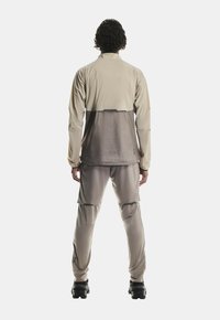 Completo da ginnastica beige composto da giacca e pantaloni con una parte inferiore di colore più scuro; texture liscia, design minimalista e dettagli con zip.
