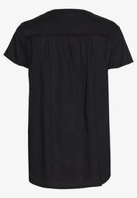 Chemise noire à manches courtes avec une coupe ample, un dos plissé et un détail décoratif tissé sur les épaules. Texture de tissu lisse.