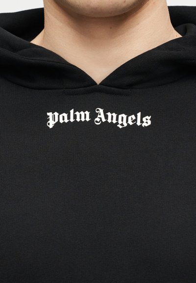 Must kapuutsiga dressipluus valge gooti stiilis "palm Angels" logoga rinnal, seljas inimesel, kelle kael ja alumine nägu on nähtavad.