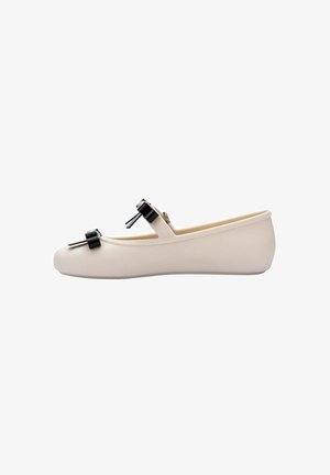 Beige Ballerinas aus glattem Material mit runder Zehenpartie. Verfügt über schwarze metallische Schleifenakzente und einen gerippten Rand für zusätzliche Textur.