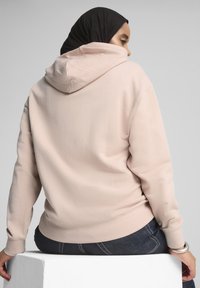 Sudadera con capucha de color rosa claro, de corte relajado, con puños y bajo acanalados. Textura suave y detalle de diseño con bolsillo canguro.