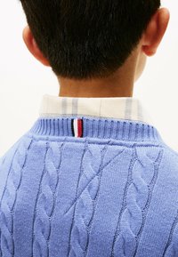 Maglione azzurro a trecce con colletto a coste, dotato di un colletto sottostante bianco e a righe e un accento a righe sul retro.