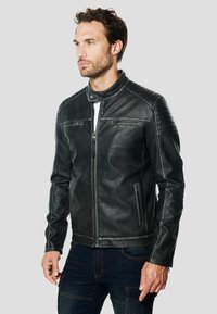 Zwarte leren jas met een hoge kraag, een rits aan de voorkant en geribbelde accenten op de schouders. Voorzien van twee zakken met rits en een gestructureerde afwerking.