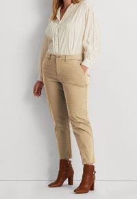 Beige chinos with a slim fit and side pockets, paired with a light cream, textured blouse, and brown ankle boots with a block heel.