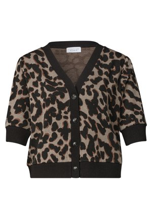 Kvinde med skulderlangt blondt hår iført en kortærmet leopardmønstret sweater og blå jeans, vendt mod venstre foran en ensfarvet baggrund.