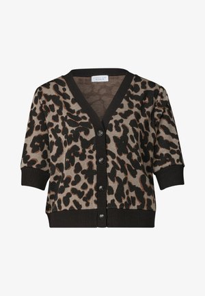 Kvinde med skulderlangt blondt hår iført en kortærmet leopardmønstret sweater og blå jeans, vendt mod venstre foran en ensfarvet baggrund.