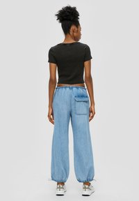 Černý žebrovaný crop top, světle modré široké džíny s elastickými manžetami a zadní kapsou, spárované s bílými teniskami.