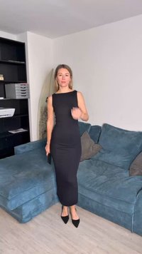 Melnā cieši pieguļošā kleita ar kvadrātveida izgriezumu, potīšu garumā, izgatavota no gludas auduma. Nēsāta ar melniem uzpurnīšiem un turēta ar clutch somiņu.