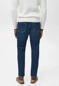 Dunkelblaue Jeans aus Denim mit geradem Schnitt, Fünf-Taschen-Design, sichtbaren Nähten und strukturiertem Aussehen, getragen mit braunen Sandalen.