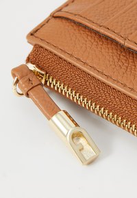 Braune Lederbörse mit strukturiertem Finish, goldfarbener Reißverschlussakzent und einem glatten Reißverschlusspull mit dekorativem Gravurdetail.