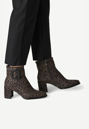 Bottines avec imprimé léopard marron et noir, talons blocs, fermetures éclairs latérales et boucles décoratives portées avec un pantalon noir.