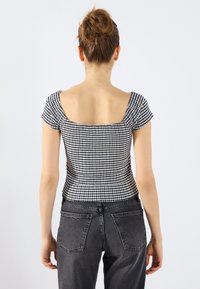 Svart og hvit rutete kortermet topp med firkantet hals. Tett passform, rillet tekstur, kombinert med høy midje svarte jeans.