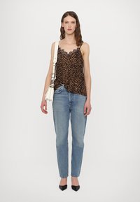 Mouwloze top met luipaardprint en kantafwerking, gecombineerd met lichtblauwe rechtzake jeans en zwarte puntige schoenen. Handtas met band.