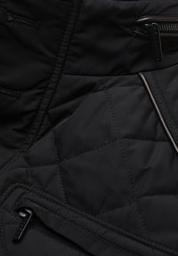 Nahaufnahme von schwarzem gesteppte Stoff mit Nähdetails und zwei schwarzen Reißverschlussanhängern an einer Jacke oder Tasche.