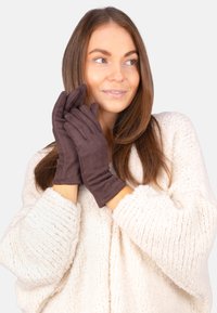 Braune Wildlederhandschuhe mit glatter Textur, tailliertem Design und dezenten Nähten. Kombiniert mit einem gemütlichen weißen Strickpullover.