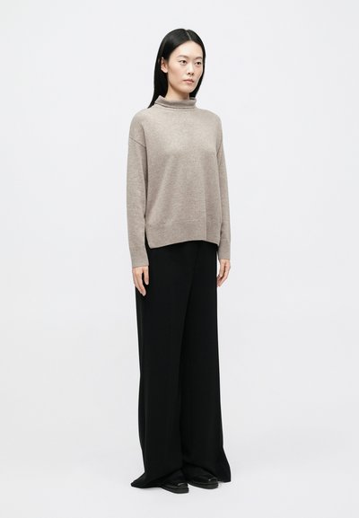 Ελαφρώς μπεζ πλεκτό πουλόβερ με ψηλό γιακά, χαλαρή εφαρμογή και ριμπ μανσέτες, σε συνδυασμό με φαρδιά μαύρη παντελόνα και μαύρα φλατ παπούτσια.