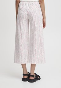 Pantalons larges blancs avec un motif rayé vertical rouge et rose. Taille élastique et détail de poche arrière, associés à des sandales noires.