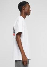 T-shirt en coton blanc à manches courtes, avec un graphique en noir et blanc au dos et du texte rouge, coupe standard, texture douce.