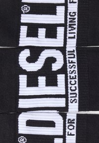 Fekete elasztikus szalag vastag fehér betűkkel: „DIESEL” és „FOR SUCCESSFUL LIVING”, texturált csíkokkal és egy kis logórészlettel.