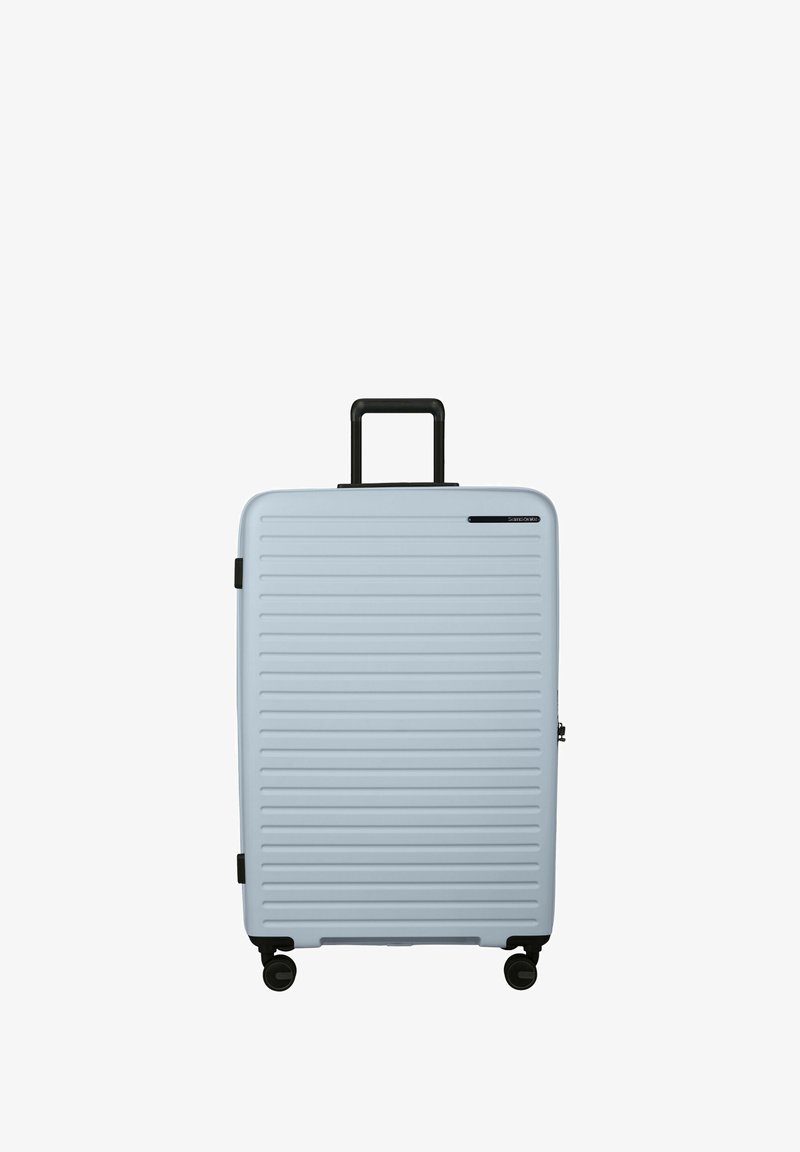 Hard-shell suitcase in light blue, featuring horizontal ribbed design, black wheels, and a retractable handle. Minimal branding detail.
