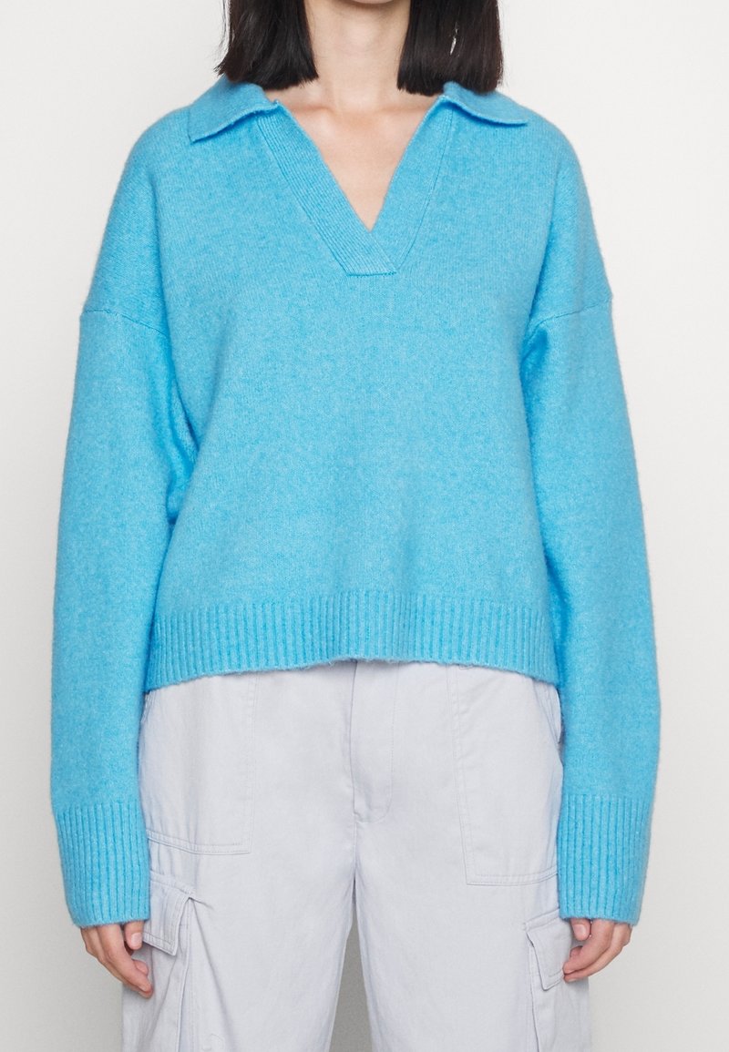 Hellblauer Strickpullover mit V-Ausschnitt und einem gerippten Saum. Verfügt über einen klassischen Kragen und eine lockere Passform. Kombiniert mit hellen Cargohosen.