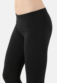 Black leggings with a wide, foldable waistband, made of stretchy, smooth fabric. Features a fitted silhouette and seamless design.