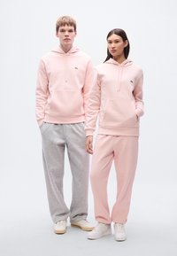 Ροζ φούτερ με κουκούλα από απαλό ύφασμα και τσέπες καγκουρό, σε συνδυασμό με ανοιχτό γκρι φόρμες. Και οι δύο εμφανίσεις έχουν απλά σχέδια και άνετη εφαρμογή.