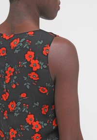 Person in einem ärmellosen schwarzen Kleid mit rot-grünem Blumenmuster, Ansicht, die Schultern und oberen Rücken zeigt.