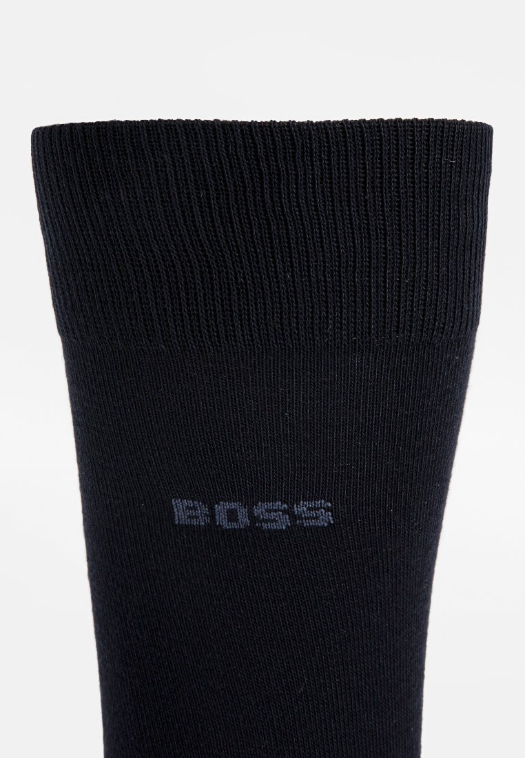 Calzino nero a coste con una texture solida. Presenta un logo grigio vicino al risvolto, progettato per comfort e durata.