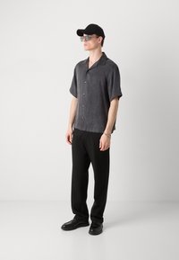 Camisa gris de manga corta con cuello, pantalones negros y zapatos negros. Los accesorios incluyen gafas de sol y una gorra de béisbol.