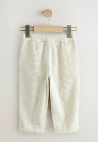 Pantaloni in velluto a coste chiari pendono da una clip di legno su un'esposizione minimalista, con coste verticali e una vita elastica.