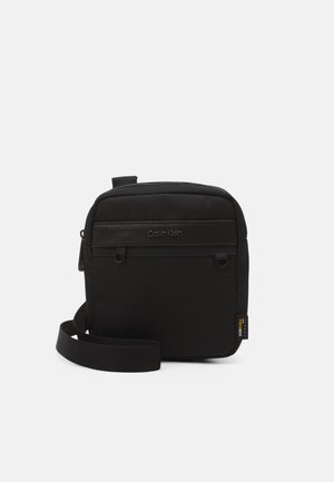 Borsa a tracolla nera con tessuto textured, chiusura con zip superiore, tracolla regolabile e dettaglio del logo impresso sulla parte frontale.