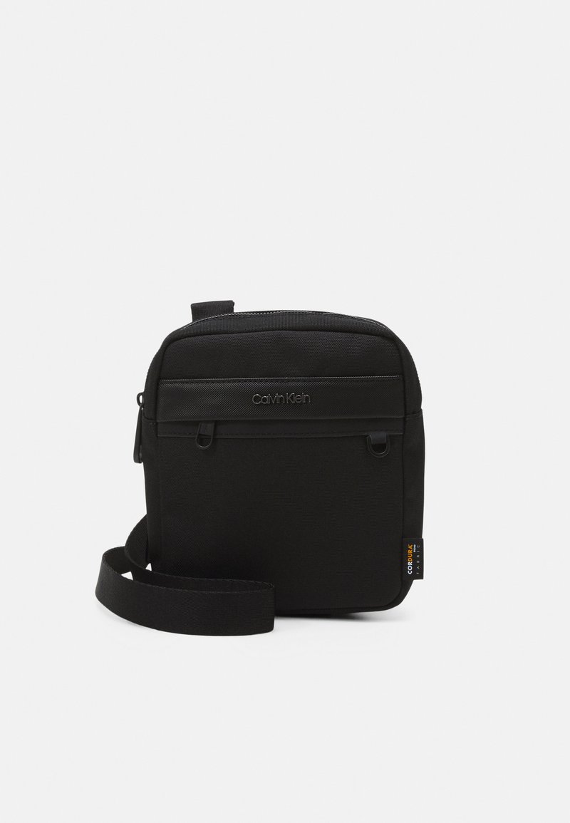 Borsa a tracolla nera con tessuto textured, chiusura con zip superiore, tracolla regolabile e dettaglio del logo impresso sulla parte frontale.