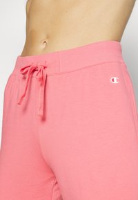 Rosa Baumwoll-Jogginghosen mit elastischem Bund, Kordelzugverschluss und weißen Logo-Details am linken Bein. Glatte Textur, bequeme Passform.