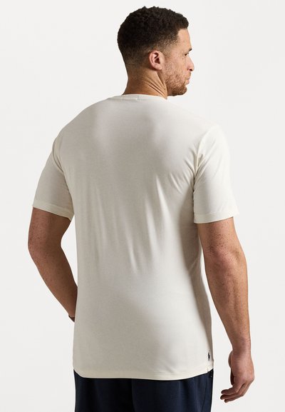 Krátký rukáv krémového trička z hladké, lehké látky s kulatým výstřihem a logem poblíž lemu. Jednoduchý, přiléhavý design.