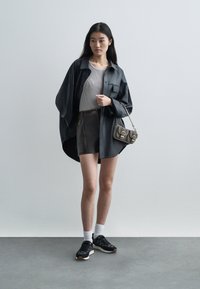 Čierna nadmerne veľká kožená košeľa, svetlo šedý priliehavý top, tmavá minisukňa s zipsovými doplnkami, čierne tenisky a malá vzorovaná kabelka.