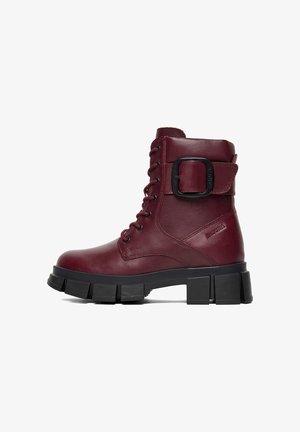 Bordeauxroter Lederstiefelette mit robuster schwarzer massiver Sohle, Schnürung vorne und seitlicher Schnallendetail für zusätzlichen Halt.