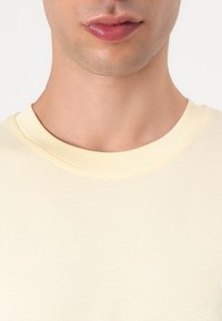 Light yellow cotton t-shirt with a crew neckline, featuring a smooth texture and subtle stitching detail around the collar and hem.