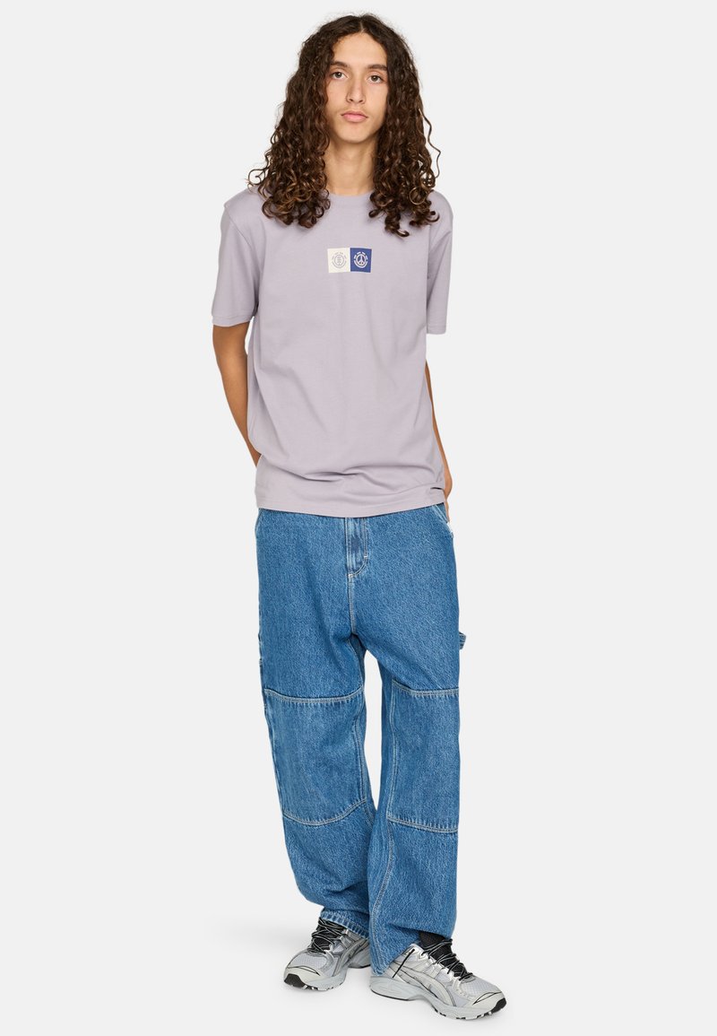 Lichtpaarse t-shirt met een ronde hals en een afbeelding op de voorkant. Gecombineerd met oversized blauwe denim broek met patchworkdetails.
