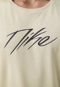 Lichtbeige mesh mouwloos shirt met een prominente zwarte Nike-logo in een gestileerd lettertype, met een ronde halslijn en een gestructureerde stof.